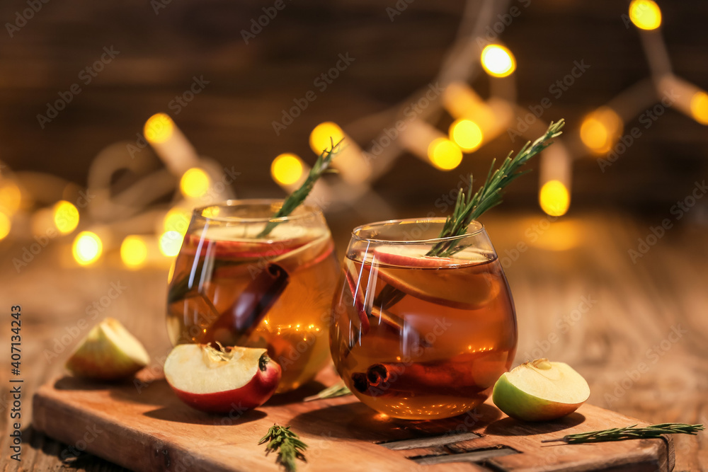 Tasty drink with spices and apple slices in glasses on wooden table at night