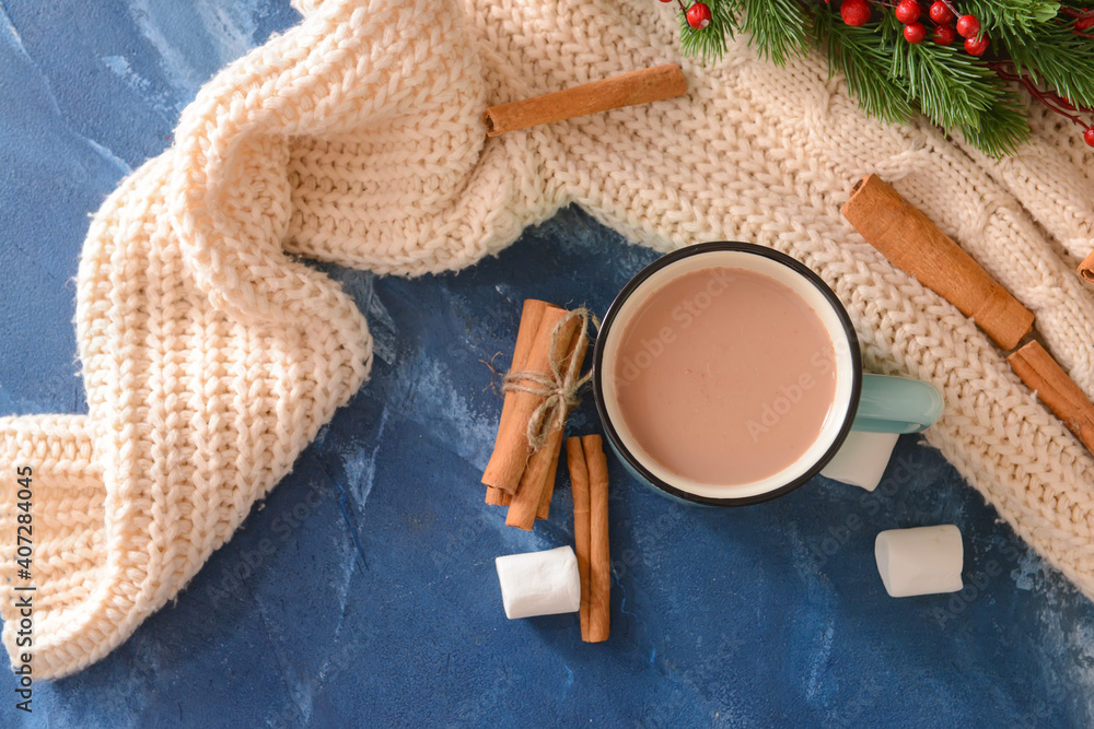 Tasty hot cocoa with cinnamon and marshmallow in cup on color background