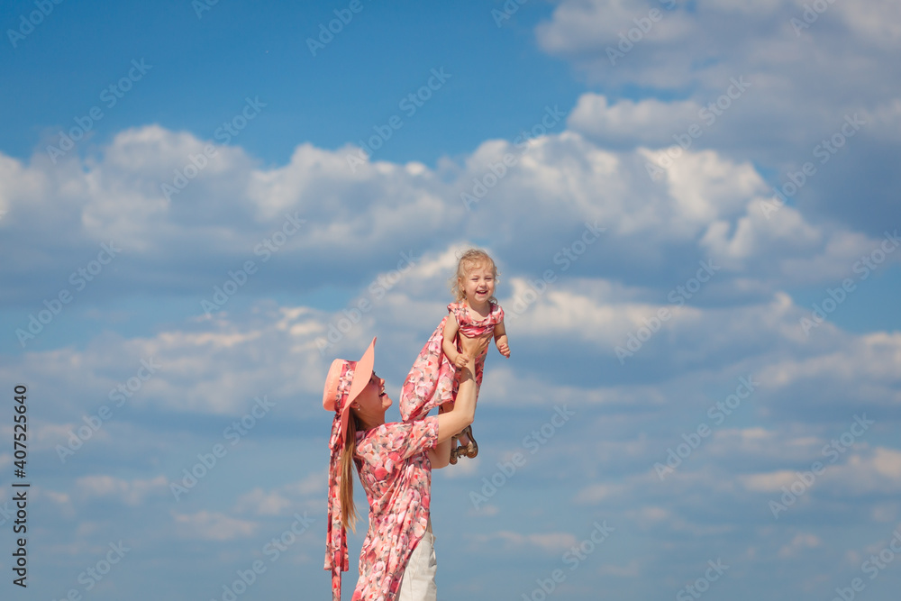 一个穿着浅色夏季太阳裙的迷人女孩和她的小女儿在沙滩上散步。很享受