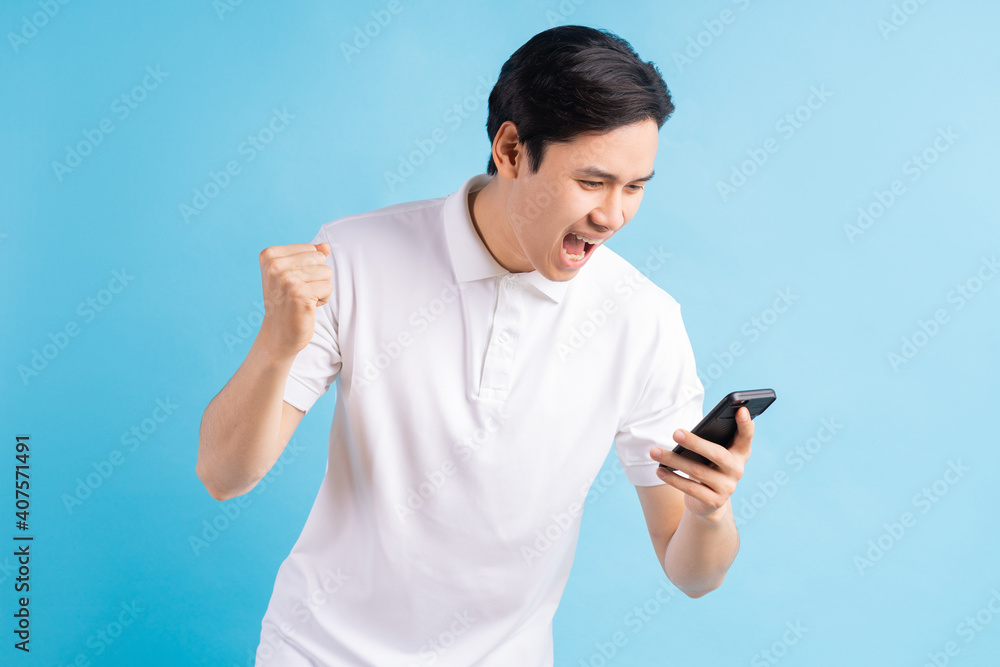 Excited handsome young male gamer playing online game on smartphone isolated on blue background