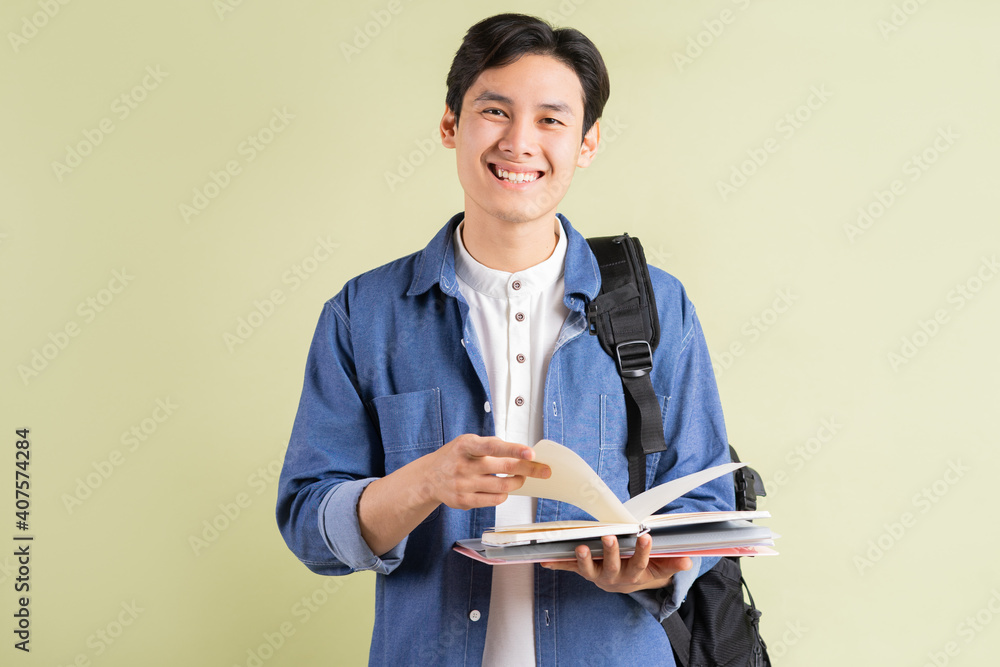 Photo of handsome Asian student smiling and holding book in hand