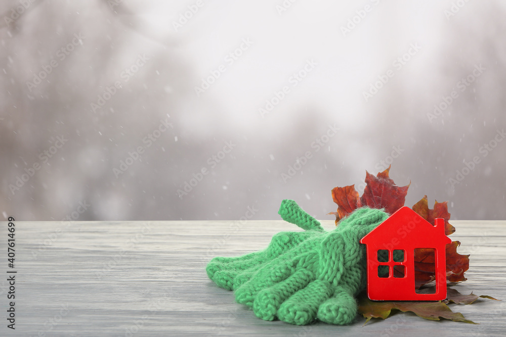 Figure of house, autumn leaves and warm gloves on table outdoors. Concept of heating season