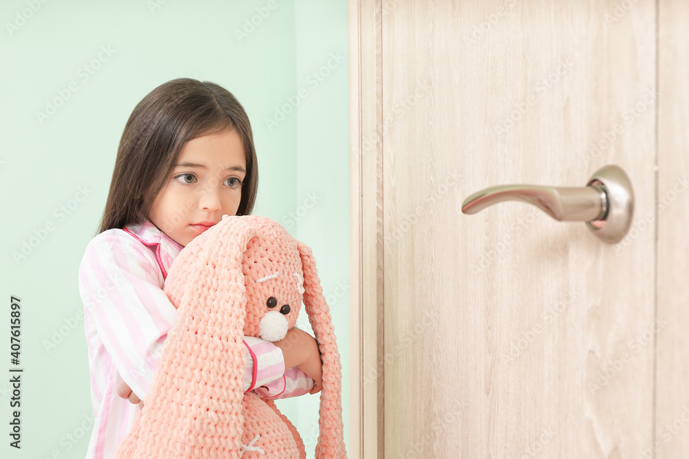 Scared little girl standing near closed door