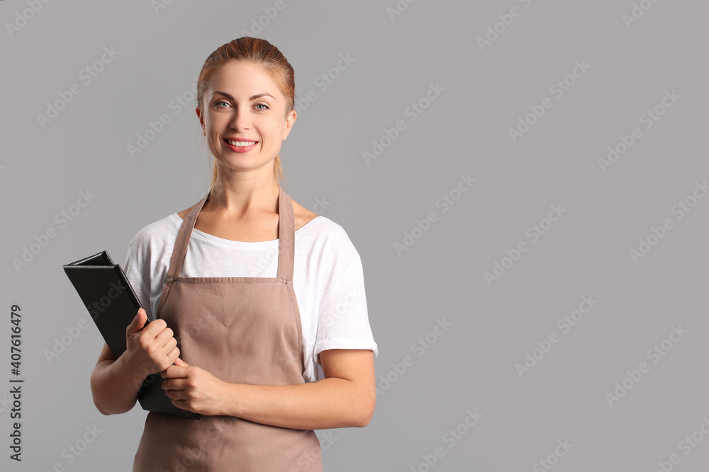 Young woman holding menu on grey background