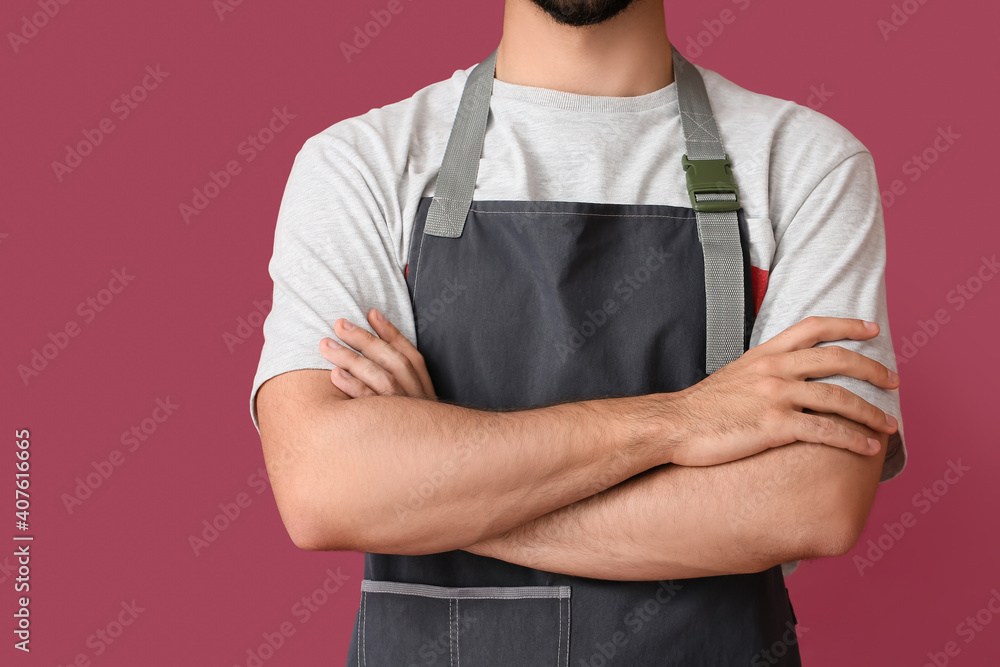 Young man wearing apron on color background