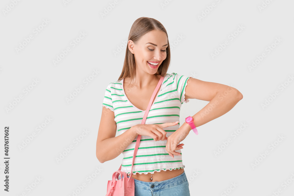 Beautiful woman looking at wristwatch on light background