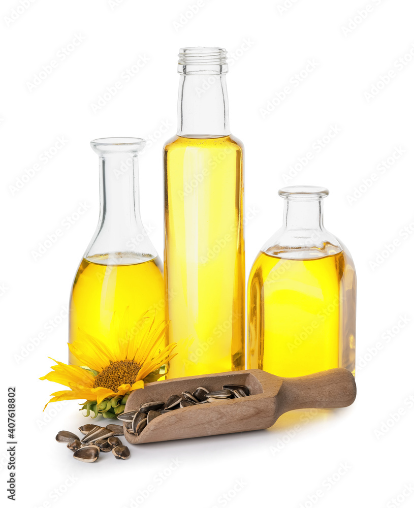 Bottles of oil, scoop with seeds and sunflower on white background