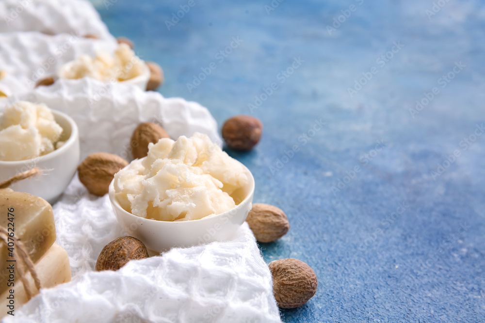 Bowls with shea butter and towel on color background