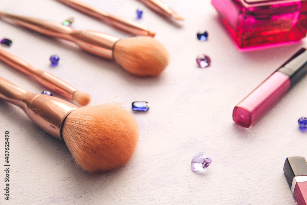 Set of makeup brushes with cosmetics on light background