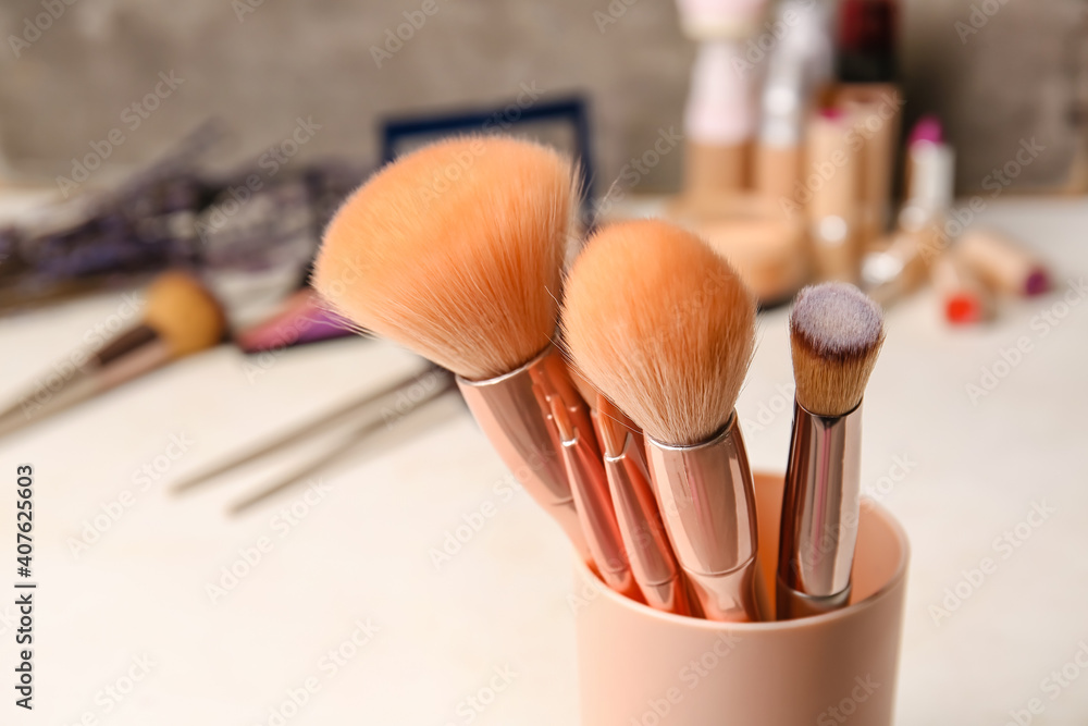 Cup with makeup brushes on table, closeup