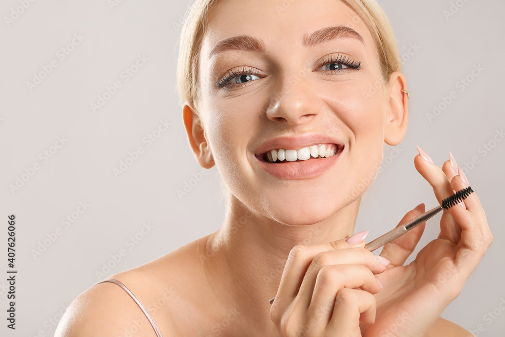 Young woman correcting her eyebrows on grey background