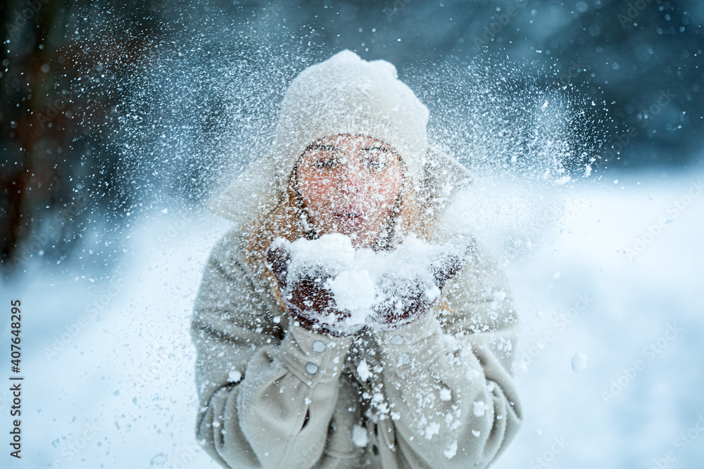 美丽的女人在雪地公园里吹雪