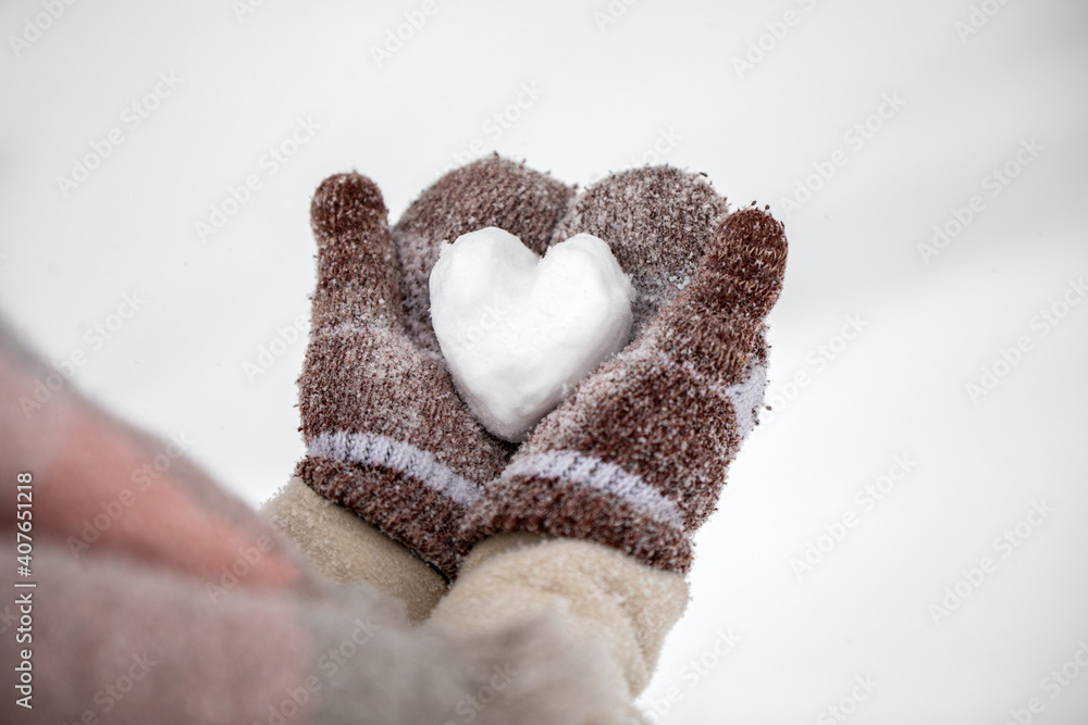 戴着针织手套的女性手在冬日里捧着一颗白雪皑皑的心