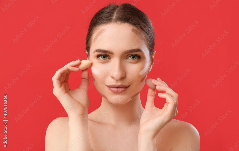 Beautiful young woman applying contouring makeup against color background