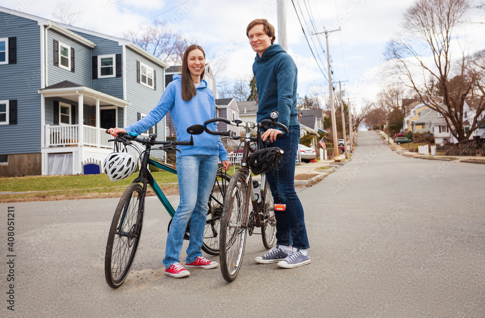 Happy young smiling couple stand with bicycles on urban street in a typical American neighborhood