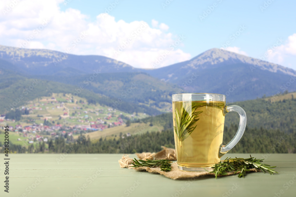 Cup of hot tea with rosemary on table in mountains