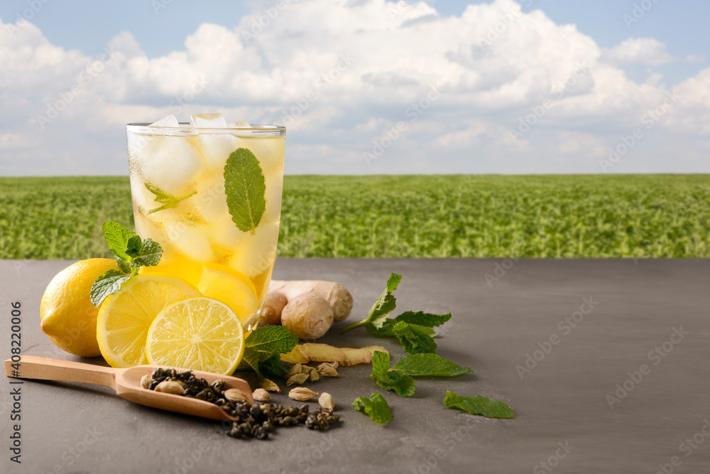 Glass of cold lemon tea and ginger on table in field