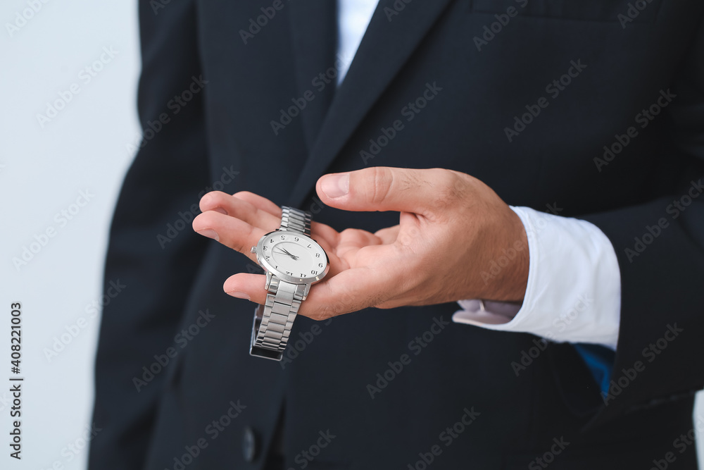 Young businessman holding stylish wristwatch on light background