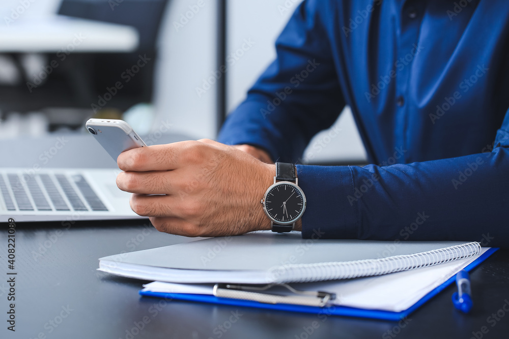 Handsome businessman with stylish wristwatch and mobile phone in office