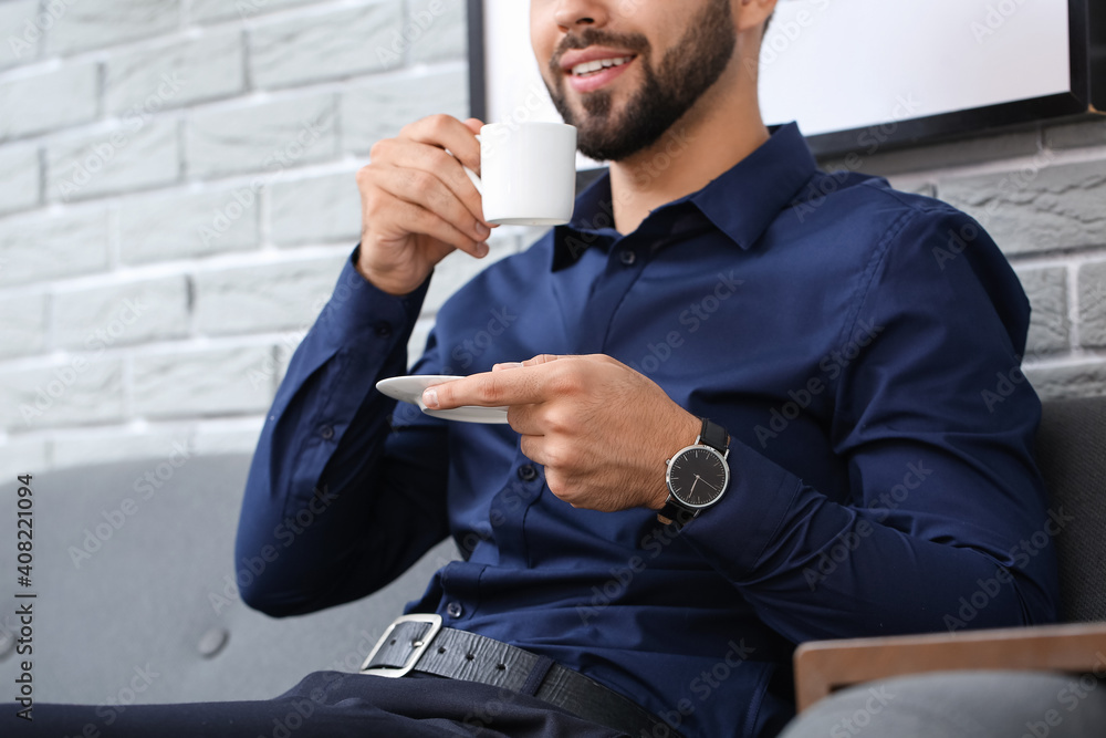 Handsome businessman with wristwatch drinking coffee in office