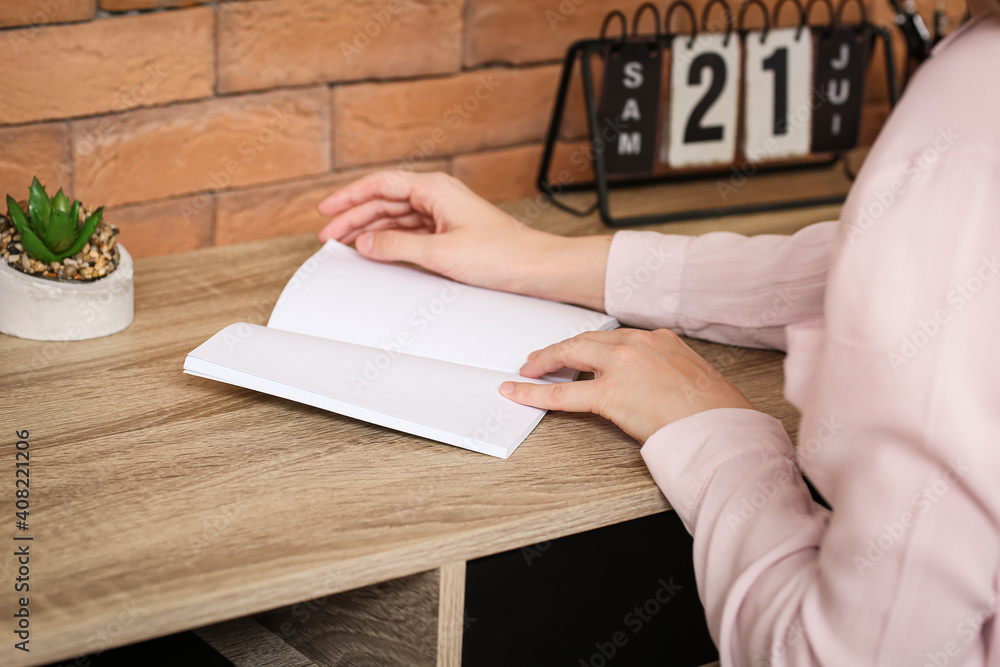 Young woman reading blank book on table in room