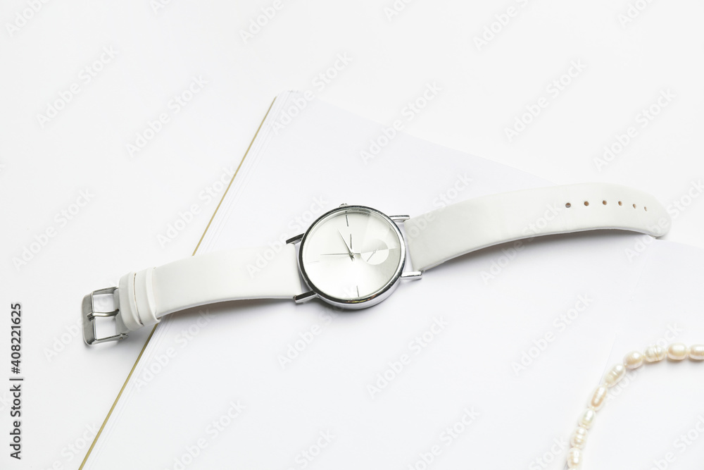 Stylish wristwatch and necklace on white background