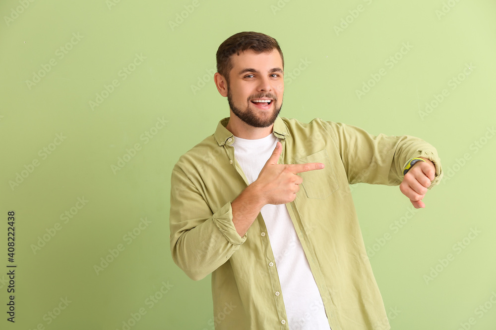 Handsome man pointing at wristwatch on color background