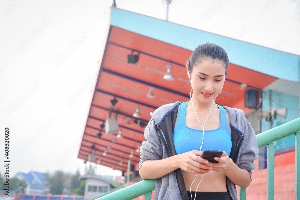 Beautiful asian woman in sportswear listening to music on earphones after exercising outdoors in the