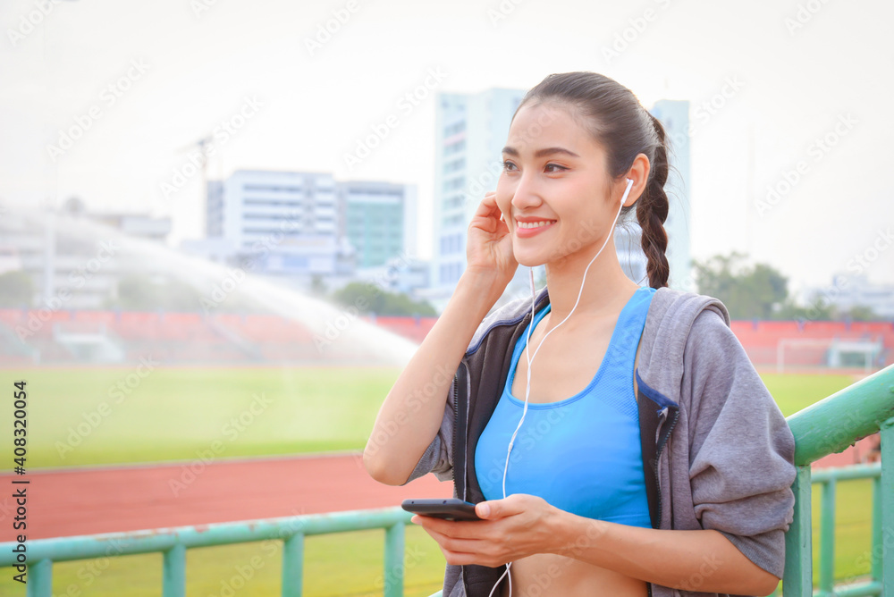 Beautiful asian woman in sportswear listening to music on earphones after exercising outdoors in the