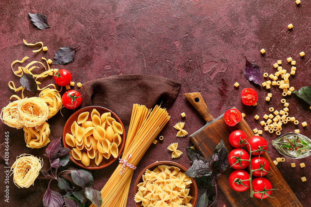 Assortment of dry pasta with herbs and tomatoes on color background