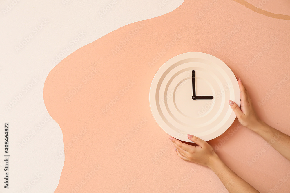 Female hands with clock on color wall