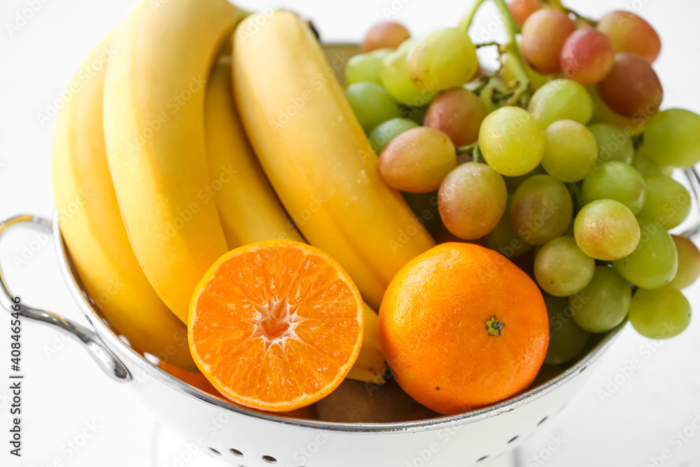 Colander with different fruits on white background, closeup