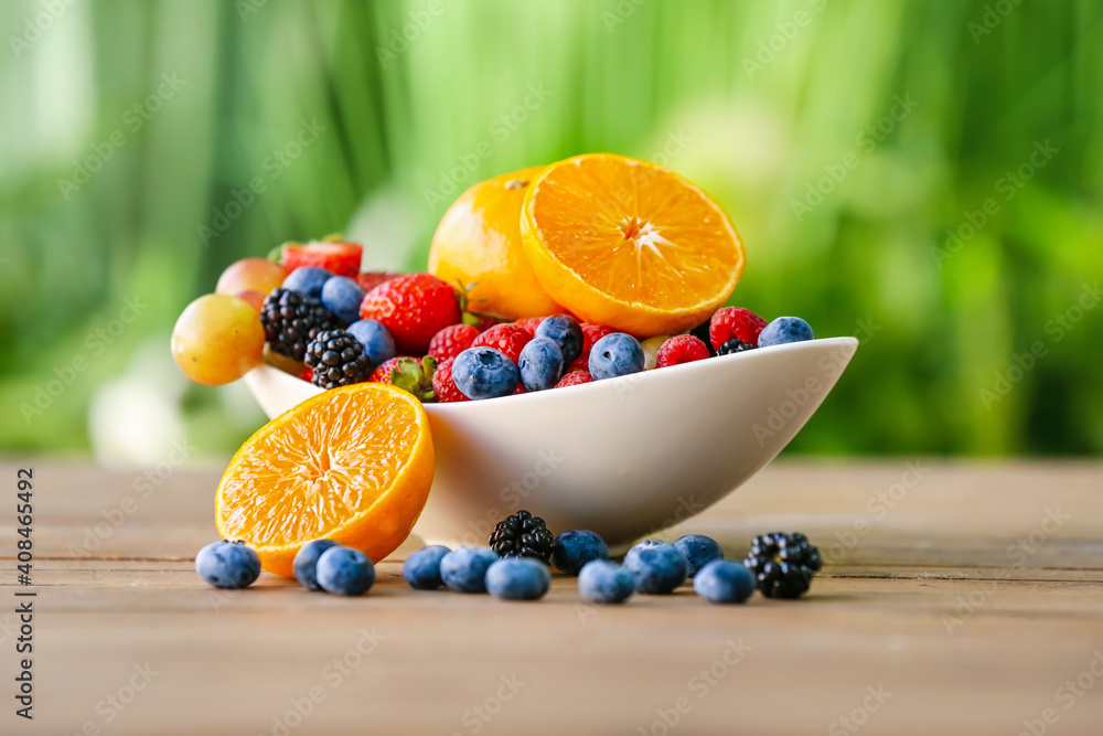 Bowl with different fruits and berries on table outdoors