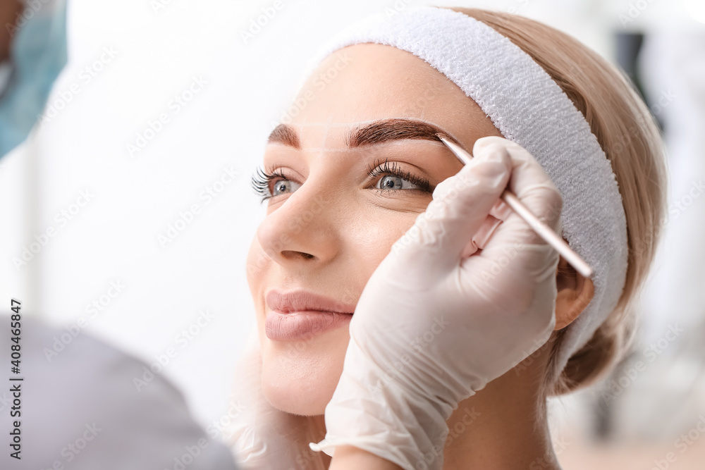 Young woman undergoing eyebrow correction procedure in beauty salon