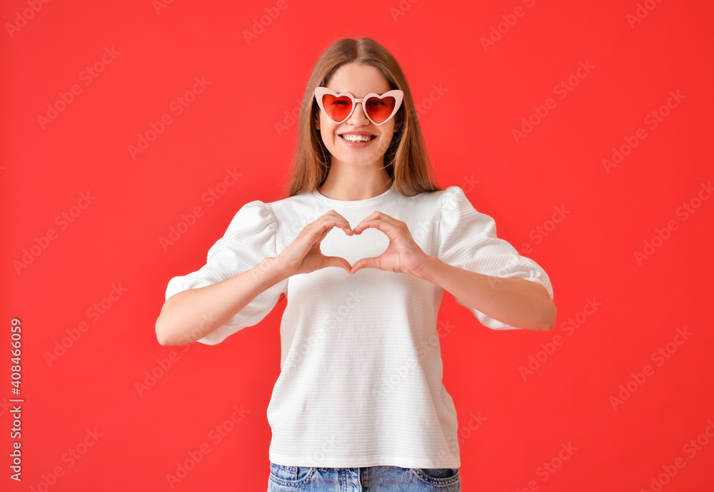 Young woman making heart with her hands on color background