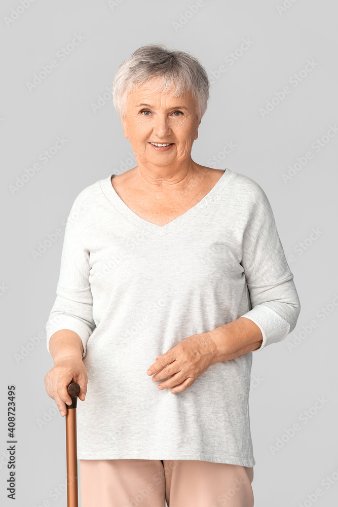 Senior woman with walking stick on light background