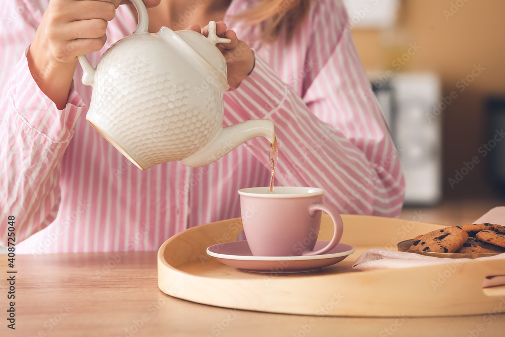 女人从桌子上杯子里的茶壶里倒茶