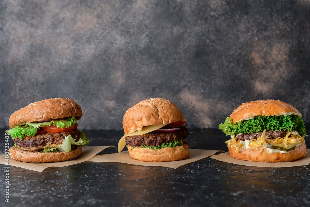 Different tasty burgers on dark background