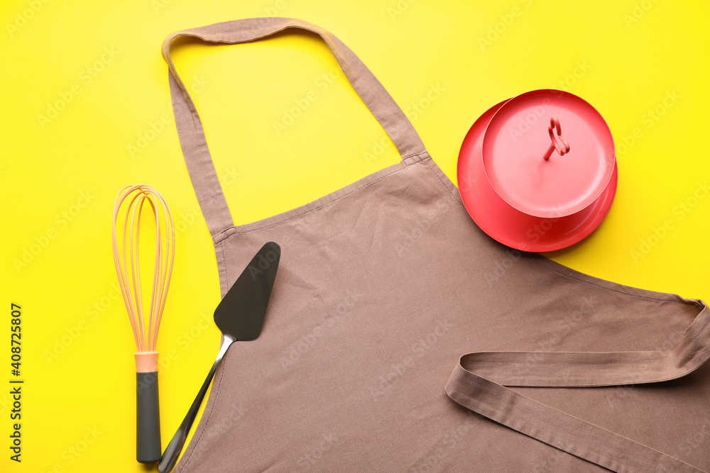 Apron and set of kitchen utensils on color background