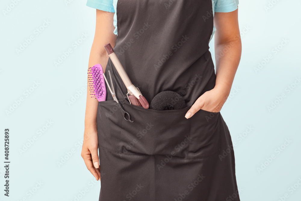 Woman wearing apron with hairdressers supplies on color background