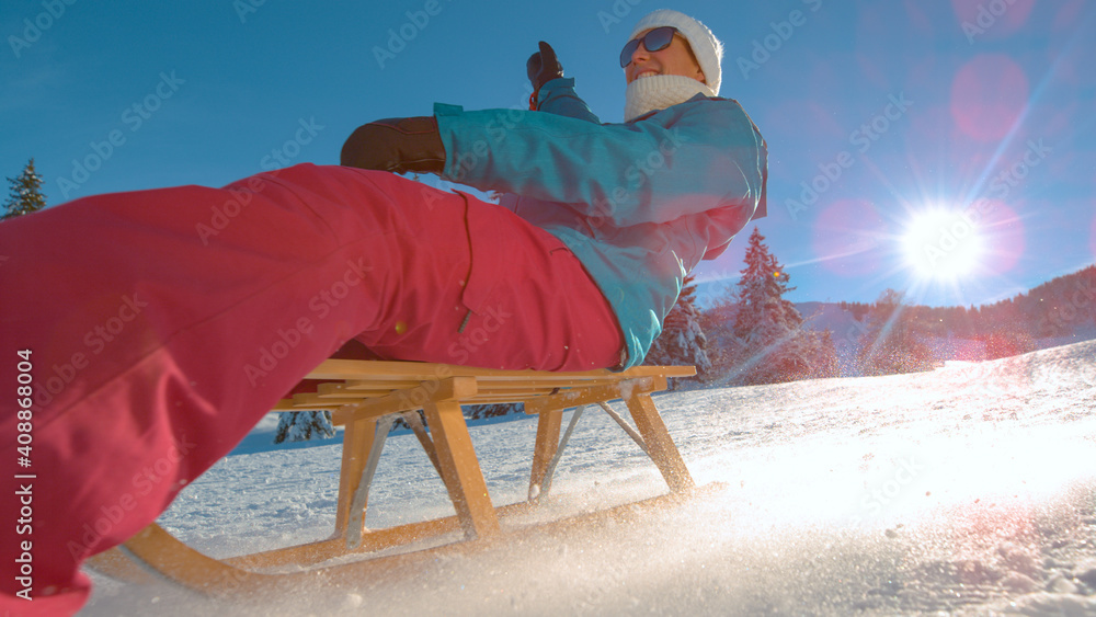 LOW ANGLE: Cheerful woman on vacation in Kranjska Gora sleds down snowy hill.