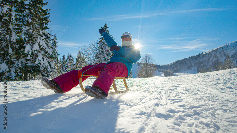 阳光明媚的日子里，一名低角度女子在滑雪橇下雪山时伸出手臂