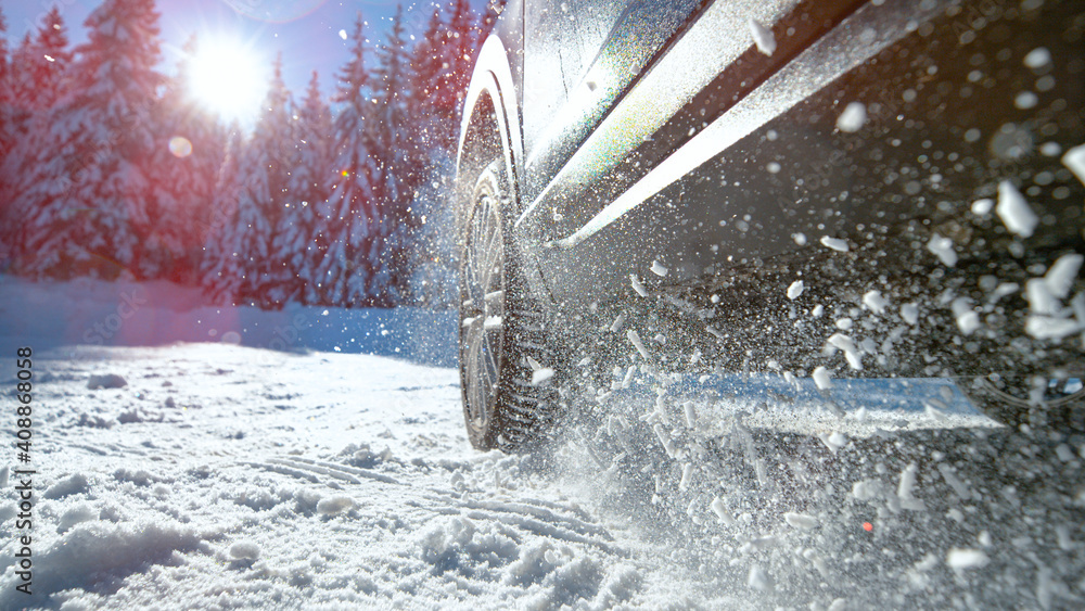 LOW ANGLE: Bright sun rays shine on car struggling to gain traction in snow.