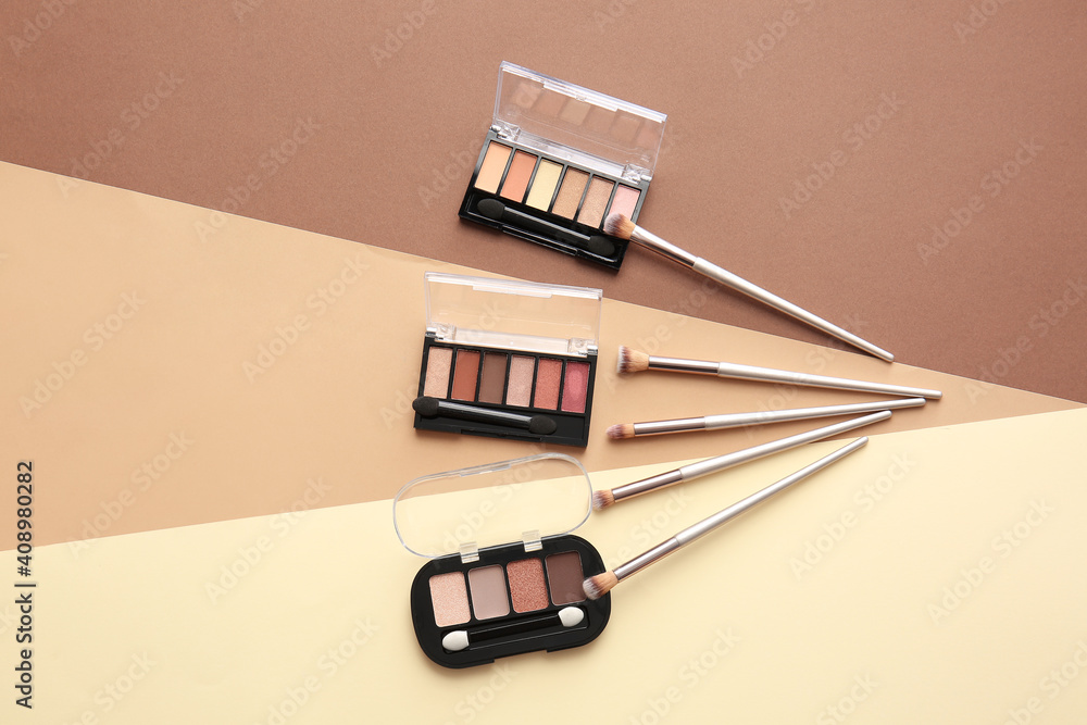 Beautiful palettes of eyeshadows and brushes on color background