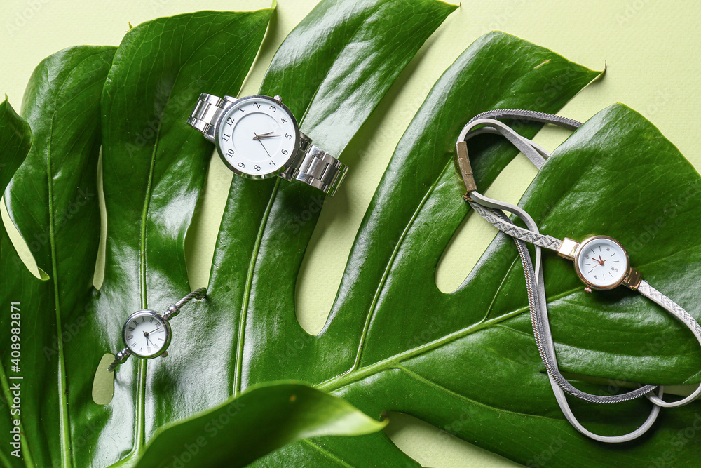 Composition with stylish wrist watches on green leaf