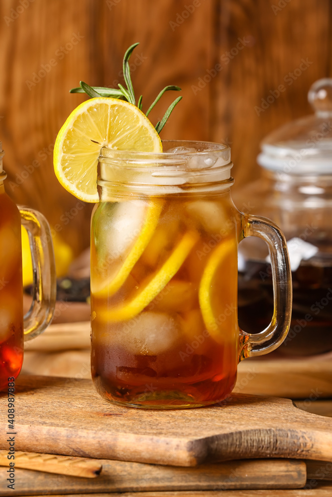 Mason jar of cold black tea with lemon on wooden background