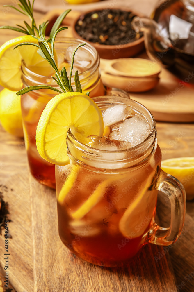 Mason jars of cold black tea with lemon on wooden background