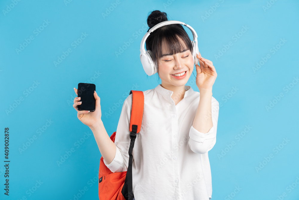 Asian female student wearing backpack behind her back, holding smartphone, neck wearing wireless ear