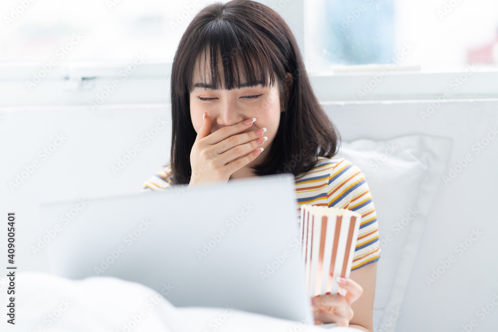 Young asian woman using laptop to watching tv shows, eating popcorn at home