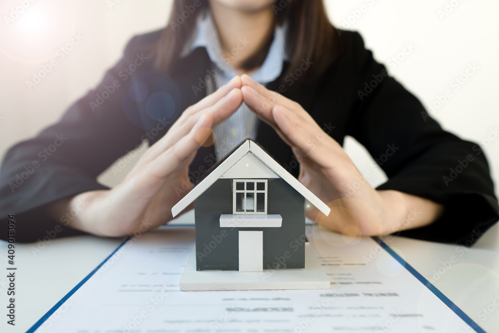 The hand of a home insurance broker protecting the small home on the desk.